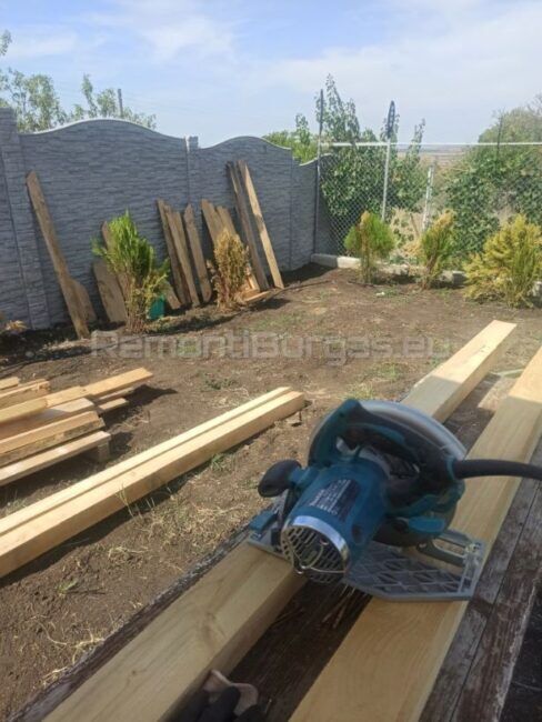 Строителен обект с дървени материали и ръчен циркуляр, подготовка за започване на нов проект за дървена детска площадка.