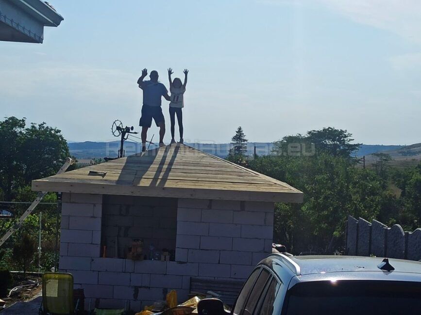 Двама човека качени на билото на нов покрив в Бургас, които забавно махат с ръце за поздрав